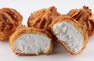 Cut in half and whole porophytroles with white cream on a white background. Eclair with cream. photo
