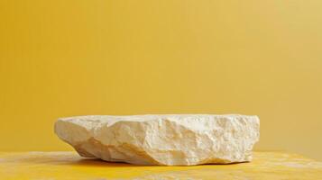 A large, rough stone with a natural textured surface sits on a yellow background, casting soft shadows in daylight. photo