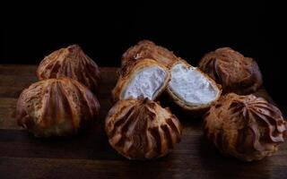 Profiteroles with white custard on a wooden board. Mini eclairs with white cream. photo