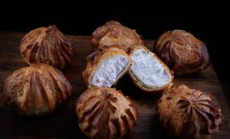 Profiteroles with white custard on a wooden board. Mini eclairs with white cream. photo