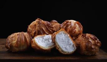 Profiteroles with white custard on a wooden board. Mini eclairs with white cream. photo