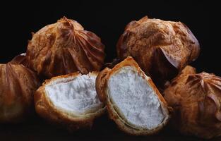 Profiteroles with white custard on a wooden board. Mini eclairs with white cream. photo