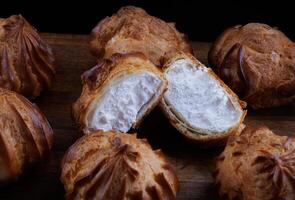 Profiteroles with white custard on a wooden board. Mini eclairs with white cream. photo