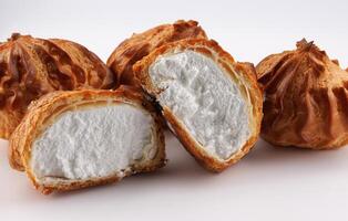 Cut in half and whole porophytroles with white cream on a white background. Eclair with cream. photo