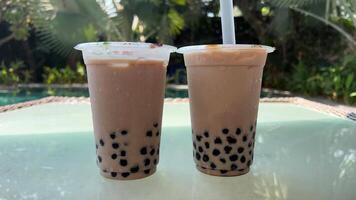 Milk bubble tea with tapioca pearls in glass, gray background. Two Bubble Tea drinks with ice and Tapioca topical balls, a large straw, stir and pierce video