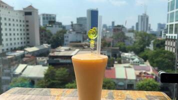 Against the backdrop of Ho Chi Minh City in a restaurant Close-up of the fresh mango juice poured in a tall glass next to a mango cut into cubes on a sunny day video