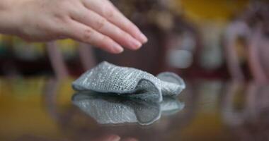 Wipe the table with a cloth cleaning a white table, wearing an apron and using a cloth to wipe the surface, the scene captures the reflection of the cleaning process on the table, with a blurred video