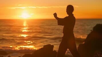 A serene silhouette of a person practicing tai chi by the ocean at sunset indicating the positive impact of mindbody activities on brain health photo