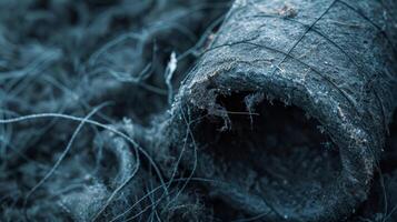 A detailed view of a dark gray material hugging a large pipe with thin strands of insulation trailing off the edges photo