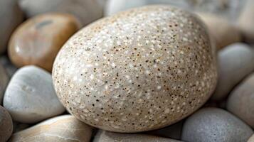 A macro shot of a small smooth river pebble with a light brown color. The surface is speckled with tiny dots creating a subtle texture photo