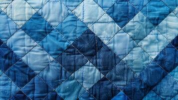 The textured fabric of a quilted blanket shows a repeating pattern of quilted diamonds in various shades of blue photo