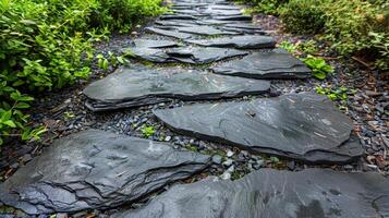 A row of rough irregularly shaped slate stones p side by side to form a straight and narrow path adding a rustic touch to the surrounding greenery photo