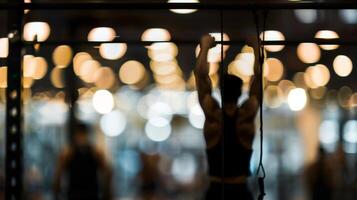 Blurry silhouette of a person hanging from a pullup bar in a dimly lit gym surrounded by other blurred figures engaged in various corestrengthening exercises at the Core Strength Center. photo