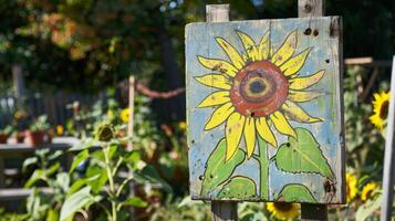 A sign with a handpainted sunflower design inviting visitors to explore the community garden photo