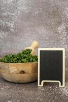 Dry parsley spice in wooden bowl with empty blackboard mock up template. Homegrown herbs and spices for cooking. Fresh dried aromatic natural food ingredients. Copy space photo