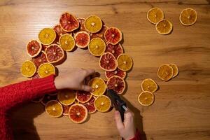 Step by step instruction of Woman using hot glue handmade Christmas wreath made of dry fruits oranges and grapefruits. Female hands creating craft homemade decor. New year celebration. Winter holidays photo