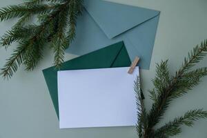 Green background with Christmas tree branch decor and copy space mock up white envelope. Template for Christmas greeting card New Year postcard. Flat lay top view photo