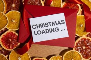 Christmas handmade wreath made of dried slices of orange and grapefruit with red envelope and paper note with CHRISTMAS LOADING... text. Winter holiday celebration greeting card. top view photo