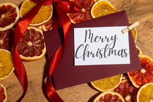 MERRY CHRISTMAS text on postcard with red envelope on dried slices of grapefruit and oranges in Christmas wreath. Zero waste eco-friendly Christmas. Sustainable greeting card decoration photo