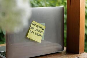 Paper note with text NO POSTING NO LIKING JUST LIVING in laptop garden background. Concept of digital detox, unplugging from technology break. Mindful living without gadgets photo