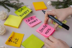 Unrecognizable woman writing new year's resolutions on colorful sticky notes. Making promises for new year, setting goals. Creating vision board motivation photo