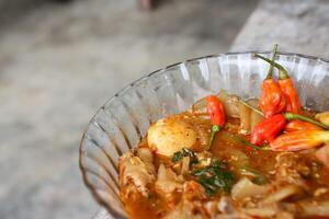 Seblak is a Indonesian dish with a savory and spicy taste. Made from wet crackers cooked with vegetables, sausage, eggs, chicken feet, seafood and processed beef. a bowl of seblak on a wooden table. photo