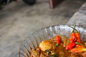 Seblak is a Indonesian dish with a savory and spicy taste. Made from wet crackers cooked with vegetables, sausage, eggs, chicken feet, seafood and processed beef. a bowl of seblak on a wooden table. photo
