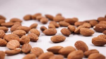 Close-up of almonds being spilled on a white background in slow motion. The nut falls from a height of about 6 inches and lands on the surface with a soft thud. frame rate of 240 frames per second video