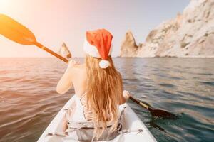 Woman in kayak back view. Happy young woman in Santa hat floating in kayak on calm sea. Summer holiday vacation and cheerful female people relaxing having fun on the boat. photo