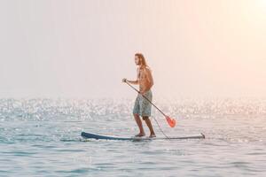 Man Sup Sea. Strong athletic man learns to paddle sup standing on board in open sea ocean on sunny day. Summer holiday vacation and travel concept. Aerial view. Slow motion photo