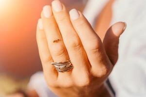 Ant walking by woman hand with a ring with feathers on her finger photo