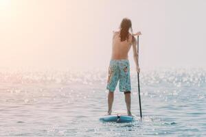 Man Sup Sea. Strong athletic man learns to paddle sup standing on board in open sea ocean on sunny day. Summer holiday vacation and travel concept. Aerial view. Slow motion photo