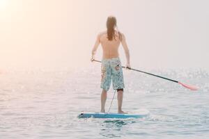 Man Sup Sea. Strong athletic man learns to paddle sup standing on board in open sea ocean on sunny day. Summer holiday vacation and travel concept. Aerial view. Slow motion photo