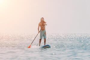 Man Sup Sea. Strong athletic man learns to paddle sup standing on board in open sea ocean on sunny day. Summer holiday vacation and travel concept. Aerial view. Slow motion photo