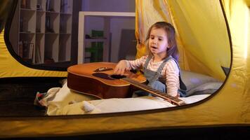 Little girl playing music on guitar. Stringed instrument in hands closeup video