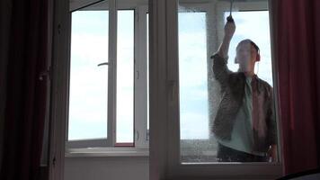 A man washes a window with a window scraper. Household chores with fun and music video