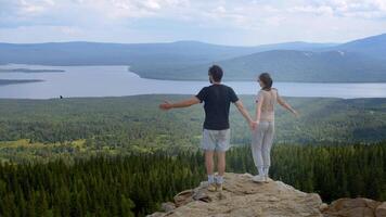 Two lovers, holding hands, approach the edge of a cliff at the summit of a mountain. They spread their arms wide and take in the magnificent natural landscape. video