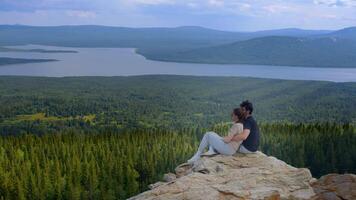 Beautiful young couple are relaxing and enjoying the breathtaking view of nature from the top of the mountain, after climbing it. video