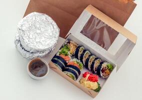 package of food from delivery stands on the table, containers with hot food packed in foil and sushi, food delivery concept photo