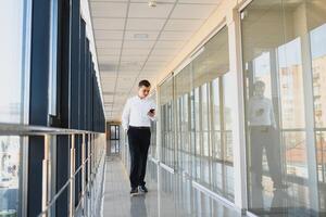Portrait of a serious confident man boss having mobile phone conversation while resting after meeting with his partners, businessman talking on cell telephone while standing in modern space indoors photo