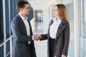 Business men and women shaking hands with a smile on the background of the large panoramic windows in a modern business center. Models dressed in a dark business suits. photo