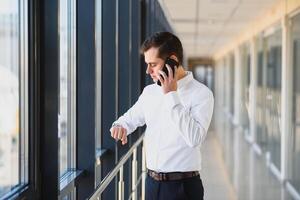 Portrait of a serious confident man boss having mobile phone conversation while resting after meeting with his partners, businessman talking on cell telephone while standing in modern space indoors photo