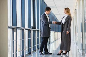 Business men and women shaking hands with a smile on the background of the large panoramic windows in a modern business center. Models dressed in a dark business suits. photo
