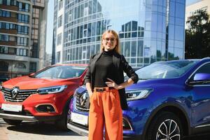Yong pretty woman standing near a big all terrain car outdoors. Driver girl in casual clothes outside her vehicle. photo