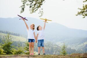 Boy and girl playing with toy airplanes on a background of mountains. Happy childhood and vacation in the mountains. photo
