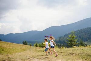 Boy and girl playing with toy airplanes on a background of mountains. Happy childhood and vacation in the mountains. photo