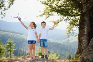 Boy and girl playing with toy airplanes on a background of mountains. Happy childhood and vacation in the mountains. photo