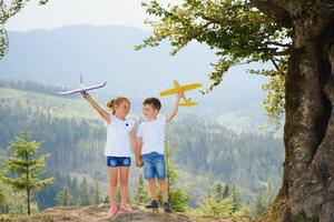 Boy and girl playing with toy airplanes on a background of mountains. Happy childhood and vacation in the mountains. photo