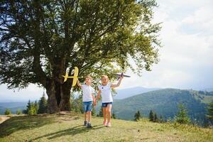 Boy and girl playing with toy airplanes on a background of mountains. Happy childhood and vacation in the mountains. photo