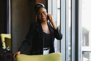 Smiling dark skinned woman in trendy wear laving cafe talking on mobile phone via roaming tariffs,african american millennial female walking and making smartphone call satisfied with connection photo